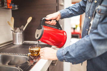 Close up focus on male hand holding kettle and pouring water into cup