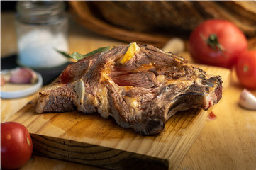 piece of entrecote on wooden board with garlic, tomatoes, bread and salt
