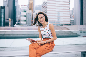 Fototapeta premium Carefree Asian woman with coffee and tablet on bench