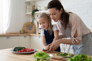 Young mother teach little preschooler daughter chop vegetables preparing salad for lunch together,...