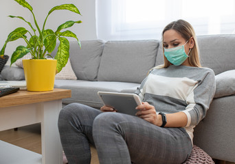 Woman using tablet on a home couch. Woman surfing on line or working from home concept. Woman at home using medical mask