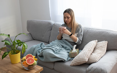 Sick woman sitting under the blanket. Sick woman with seasonal infections, flu, allergy lying in bed. Sick woman covered with a blanket lying in bed with high fever and a flu, resting and drinking tea