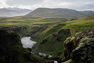 Fototapeta na wymiar Beautiful smooth river in Iceland surrounded by green hills during the sunset on the Fimmvorduhals hiking trail close to Skogar