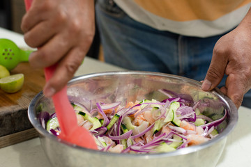 Mexican seafood made with shrimps and vegetables in a bowl is being prepared by an unrecognizable person