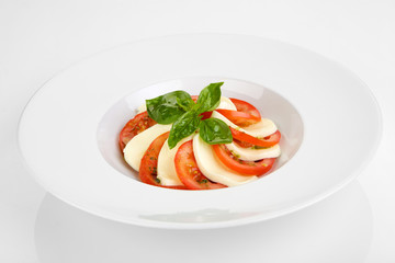 Caprese Salad with Tomatoes, Mozzarella Cheese, Rocket Salad, basil leaves, dressed with Pesto Sauce on rustic wooden background.  Traditional Italian cuisine. Flatlay healthy vegetarian dish.