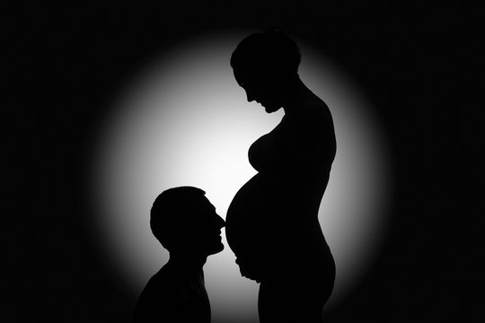 Silhouette of man kiss pregnant wife's belly. Young couple in love waiting for baby close up. silhouette man and pregnant woman. black and white portrait man and pregnant woman. 9 months of pregnancy