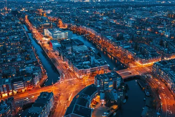 Foto auf Glas Beautiful night aerial view of Amsterdam downtown from above with many narrow canals, illuminated streets and old historic houses, drone photo. © DedMityay
