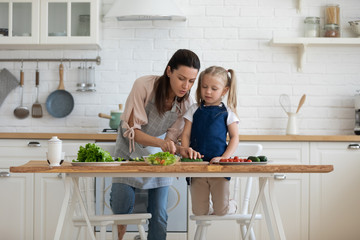 Loving young mom and cute small preschooler daughter have fun preparing food in kitchen together,...