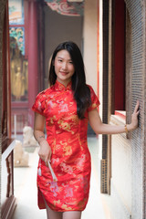 Portrait of Chinese girl wearing Chinese clothes holding paper folding fan in her hand and posing at cement door