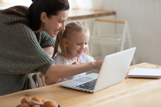 Happy Young Mother And Cute Preschooler Daughter Watch Funny Video On Laptop Together, Smiling Mom Or Nanny And Little Girl Child Have Fun Playing Game On Computer Or Studying Learning Online