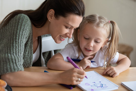 Close up of happy loving young mother enjoy playing drawing in notebook with cute little daughter, smiling mom and small girl child have fun paint pictures on paper spend weekend at home together