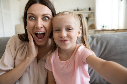Funny millennial mom or nanny have fun posing for self-portrait picture with cute little girl, overjoyed happy young mother enjoy playful weekend with small daughter, make selfie on phone together