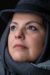 Lady head shot studio portrait. She is wearing a scarf and a hat. She is looking up.