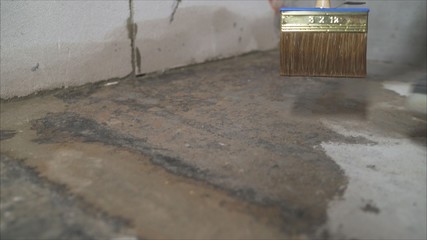 A worker moistens a concrete floor with a brush. Wet concrete floor with a brush. Stage of preparing the floor for waterproofing