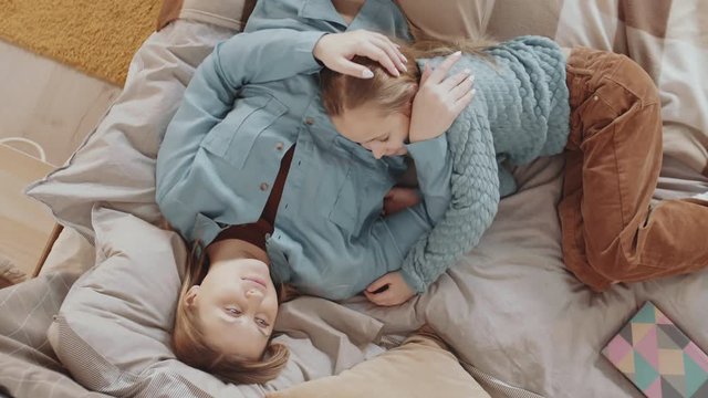 Flat lay of cute Caucasian girl and her mother lying on bed together. Woman patting girl on head