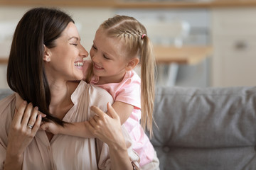 Cute little preschooler girl child hug from back young mother have fun together cuddle on couch at...