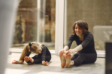 Girl is engaged in gymnastics. Family in a yoga studio. Kid in a black sportwear.