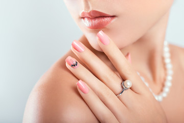 Nail art and design. Beautiful woman wearing make-up and pearl jewellery showing pink manicure with...