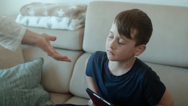 Mother scolds her son and picks up the tablet. Sad child punished and sitting on the couch