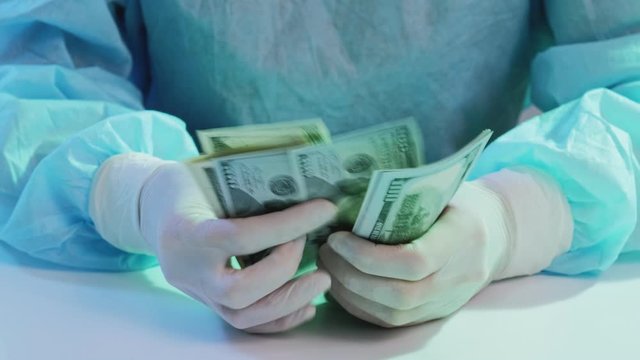 Expensive surgery. Medical payments coverage. Anesthesiologist hands counting 100 dollar bills.