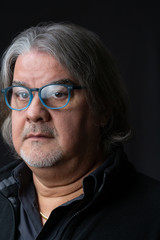 Studio head shot of man. He is serious, wearing prescription glasses and looking to the camera..