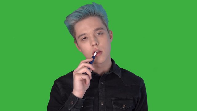 Young man smoking electronic cigarette iqos looking camera green screen