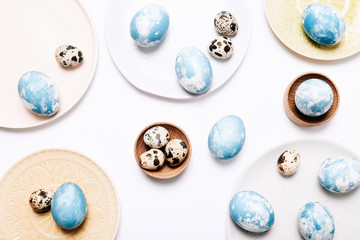 Stylish eggs with ombre blue marble stone effect in different dishes on white background