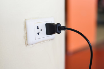 Home outlet plug is plugging socket on wall with black power cord cable - Power plug connecting...