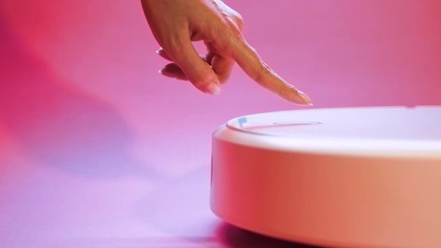Female hand presses the power button on a robot vacuum cleaner.