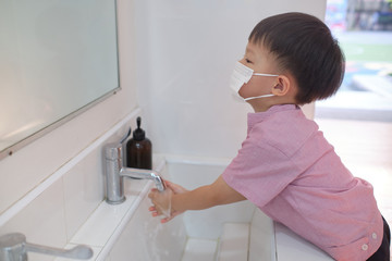 Cute little Asian 3 - 4 years old toddler boy child wearing protective medical mask washing hands...