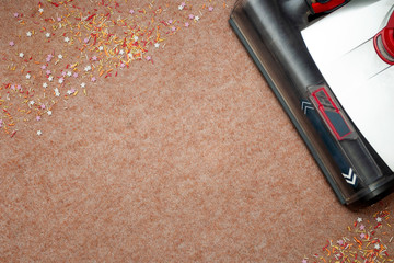 Housekeeping, doing chores and cleaning up after a party concept with vacuum cleaner sucking confetti and removing messy litter from a rug with copy space on the clean part of the carpet
