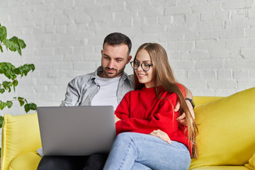 Closeup view of young cute couple looking at laptop screen siting on the yellow couch