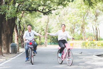 Fototapeta premium Thai Asian couples are riding bicycles in the park happily and joyfully on weekends, with clear skies, fresh air and green tree backdrop.
