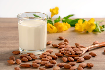 Almond milk in glass with almonds on wooden background.