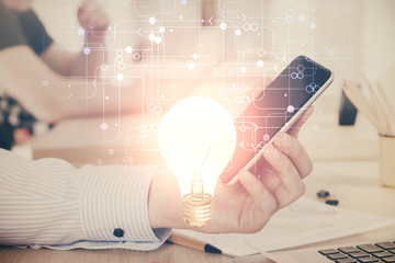 Double exposure of man's hands holding and using a digital device and bulb hologram drawing. Idea concept.