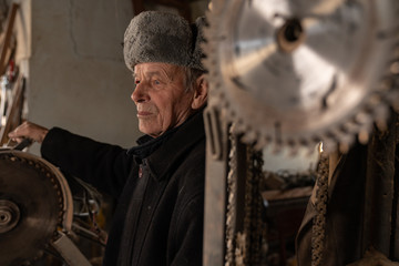 Fototapeta na wymiar Portrait of very oldsenior carpenter, he standing in his workshop and looking at left side