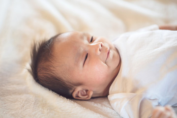 Newborn baby lying on a soft white mattress, smiling happily.