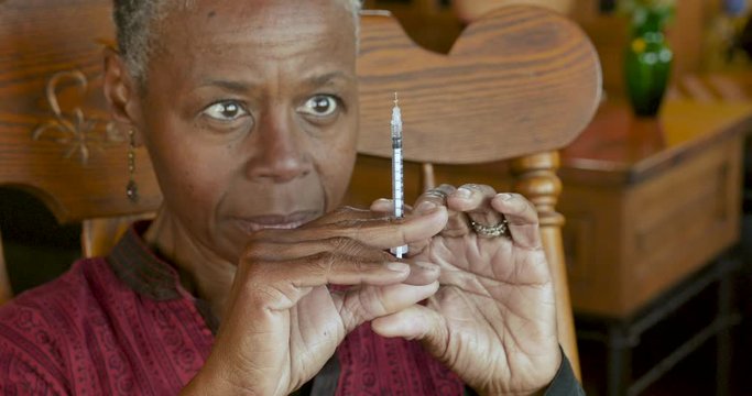 Black senior woman with a needle and syringe giving herself an injection
