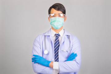 Medical doctor in white uniform doctor wears medical gloves, medical masks and and wearing protective glasses with crossed arms look at camera on gray background, corona virus concept, covid19 concept
