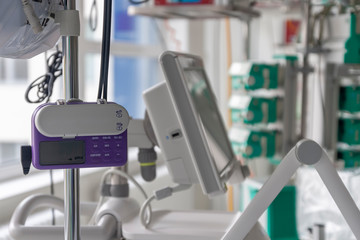 A small, lightweight, portable enteral feeding pump in ICU in hospital, on background monitor of ventilator.