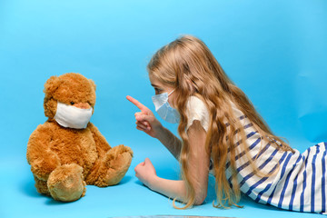 masked blonde girl talking to masked teddy bear. quarantined children concept. 