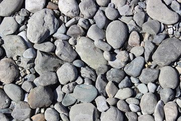 Rounded stones, pebbles, sand and rubble on the seashore. Texture