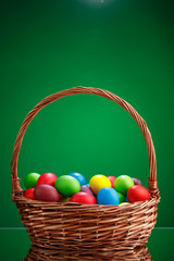 Easter color eggs in festive gift basket, green background