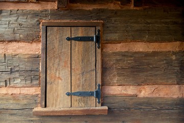 Aged wooden log cabin window, brown wood with clay and black hinges