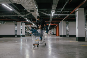 happy couple ride a trolley in an underground parking lot of a shopping center