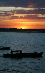 Silhueta de barco atravessando rio durante o pôr-do-sol. Céu laranja