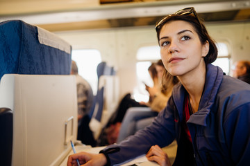 Young plane/train/bus traveler writing notes and ideas.Planing while traveling.Productivity,inspiration,writing down ideas. Arranging while flying.Ideas for a project.Freelancer