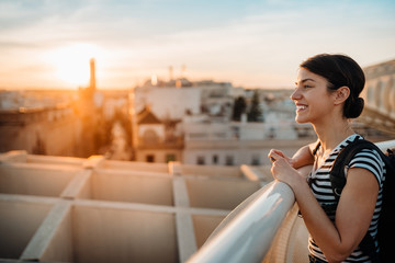Happy woman tourist enjoying sunset cityscape panorama from Seville's viewpoint.Amazed visitor having great experience traveling to Seville,Andalusia,Spain.Visiting attractions and landmarks. - obrazy, fototapety, plakaty