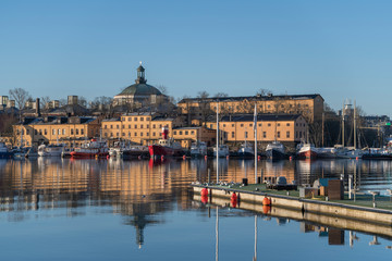 Harbor view over the old town district Gamla Stan, the islands Skeppsholmen and Blasieholmen with boats and piers in an early sunny tranquil spring day