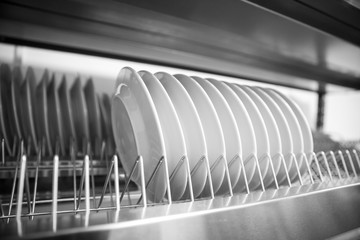 Rack steel storage of white clean dishes on shelf of professional kitchen
